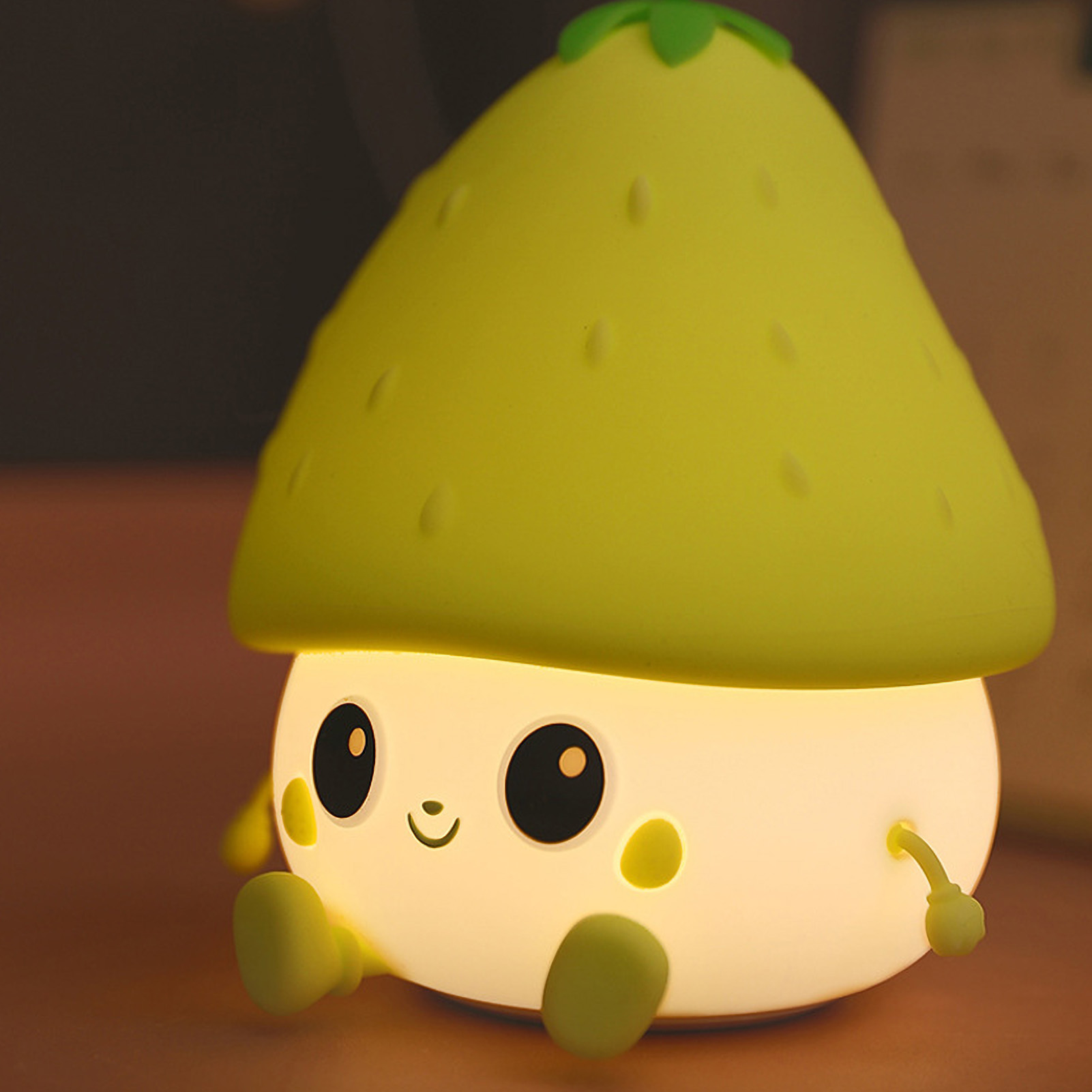 Eine kleine, leuchtende Pilzlampe mit niedlichem Gesicht, gelbem Hut und grünen Stielen sitzt auf einem Tisch.