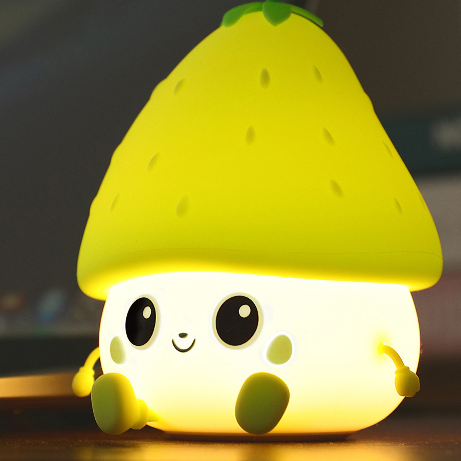 Eine niedliche, gelbe Nachtlampe in Form einer Erdbeere mit großen Augen und einem lächelnden Gesicht.