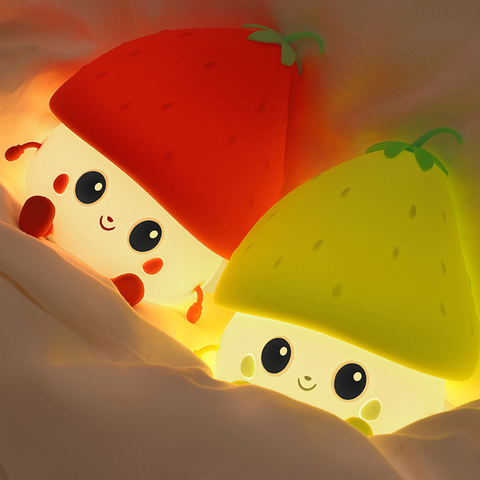 Zwei niedliche, leuchtende Erdbeer-Nachtlampen mit Gesichtern liegen im weißen Bett.