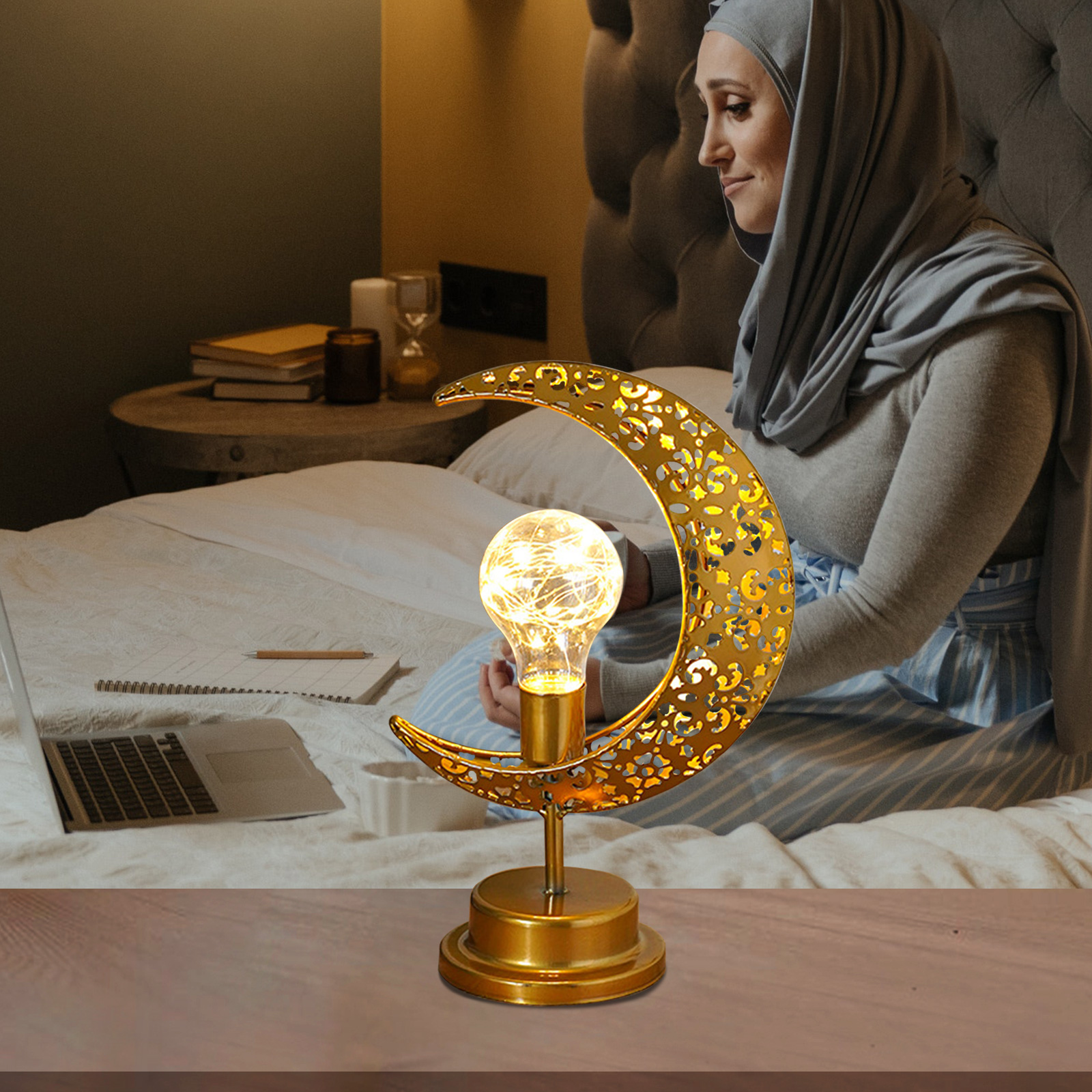 Eine Frau in grauer Kleidung sitzt auf einem Bett neben einer goldenen, mondförmigen Lampe.