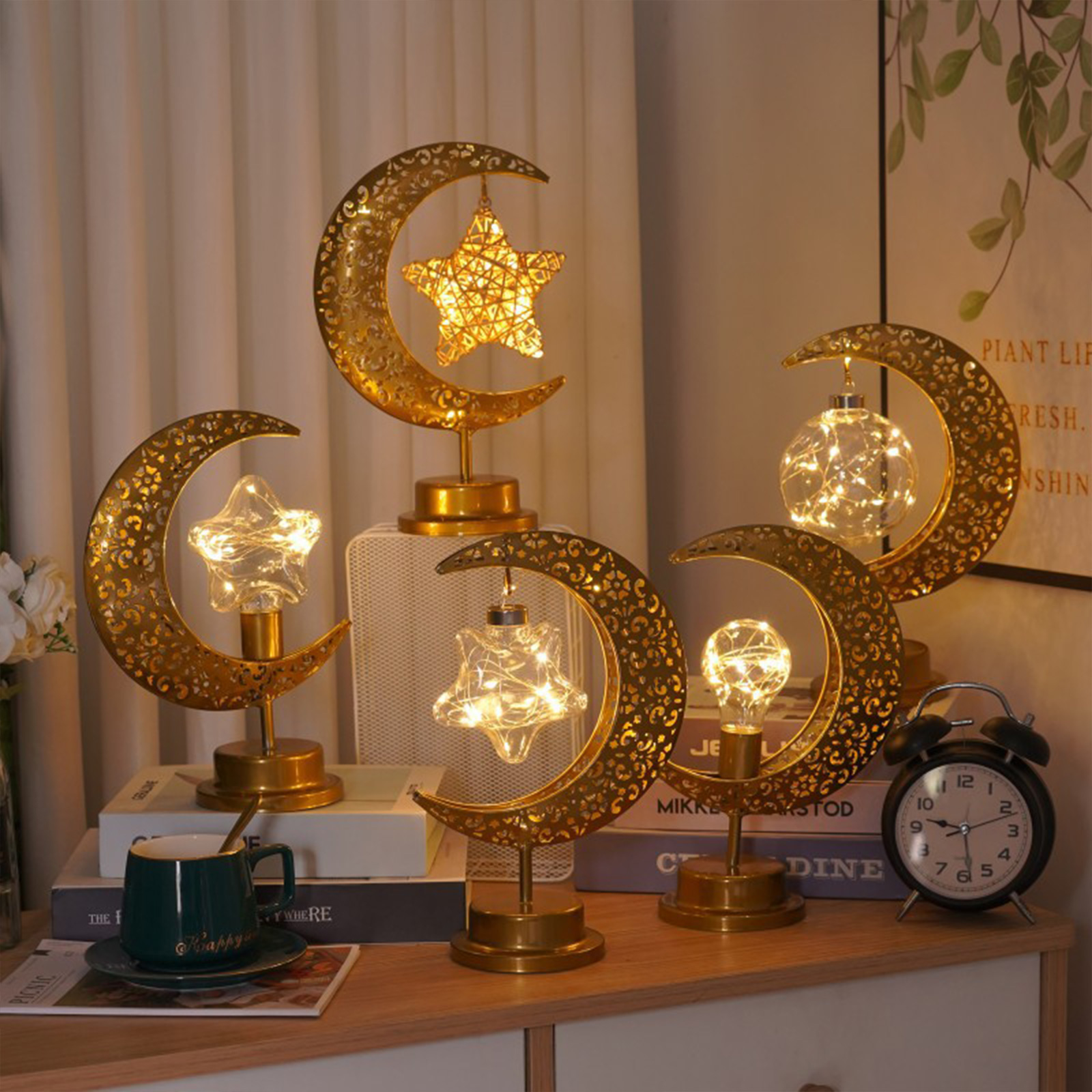 Fünf goldene Mondsichel-Lampen mit beleuchteten Sternen stehen auf Büchern neben einer Tasse.