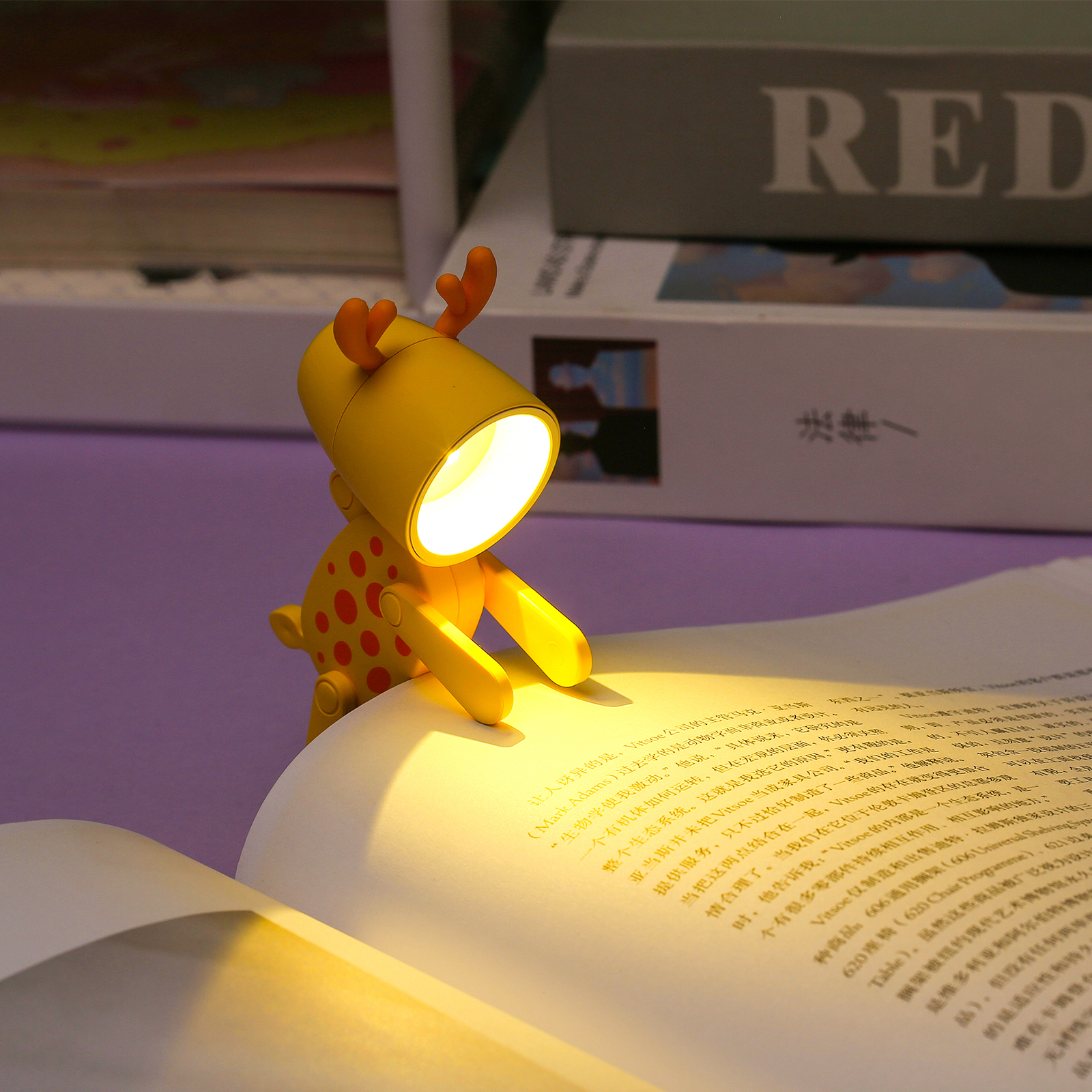 Eine gelbe, rehförmige LED-Lampe klemmt am Rand eines offenen Buches und beleuchtet die Seiten.