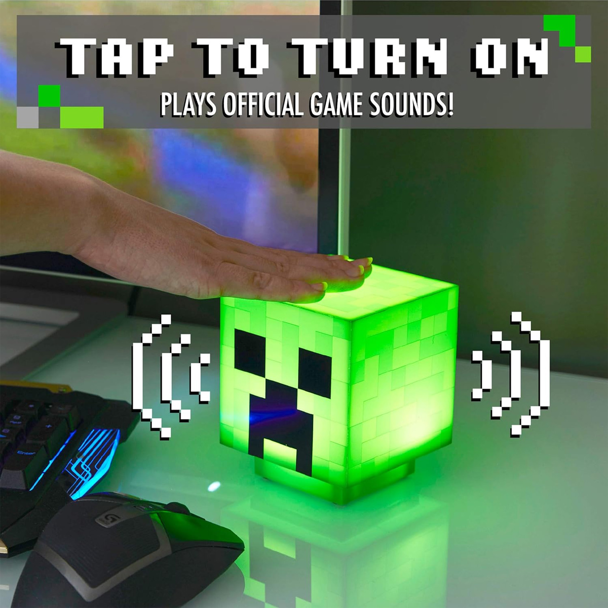 Eine Hand tippt auf eine leuchtende grüne Minecraft Creeper Würfellampe auf einem Schreibtisch.