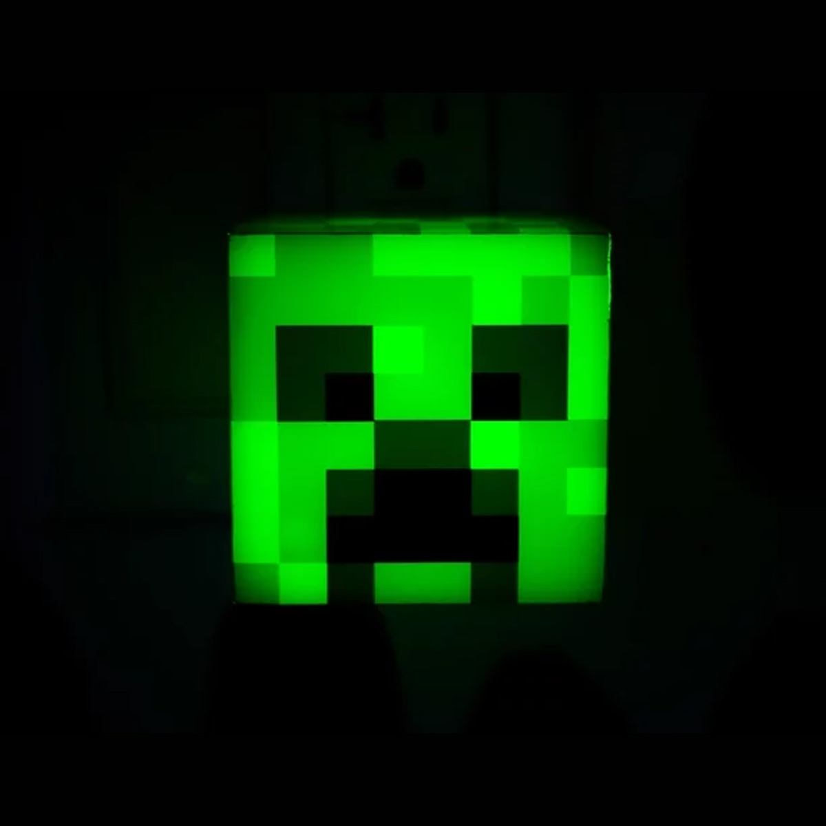 Ein leuchtend grünes Minecraft Creeper Gesicht vor dunklem Hintergrund.