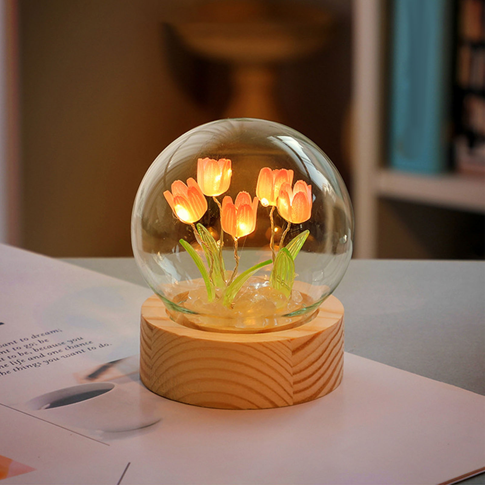 Eine leuchtende Glaskugellampe auf einem Holzsockel mit künstlichen orangen Tulpen.