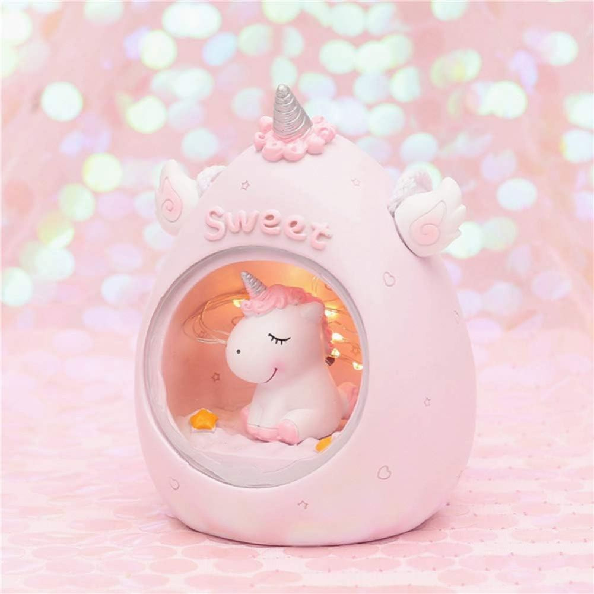 Ein rosafarbenes Einhorn-Nachtlicht mit einer kleinen Einhornfigur im Inneren vor einem glitzernden Hintergrund.
