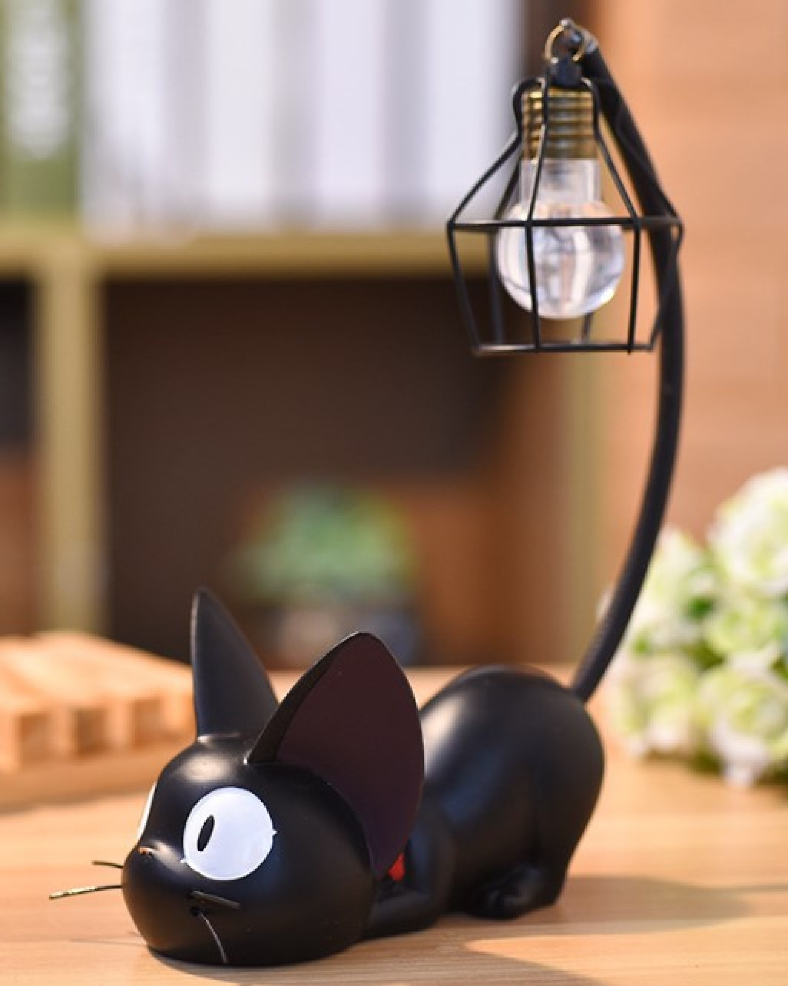 Eine schwarze Kätzchen-Figur mit großen weißen Augen und einem geschwungenen Schwanz, der eine kleine Hängelampe hält.