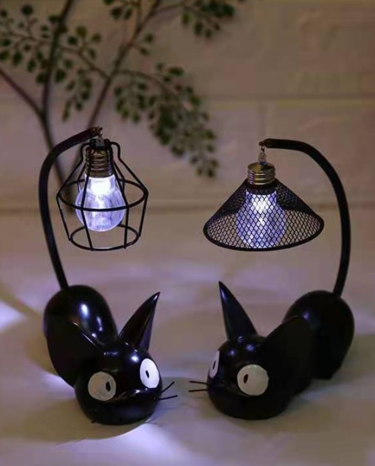 Zwei schwarze Katzenlampen mit leuchtenden Glühbirnen stehen sich auf einem Tisch gegenüber.