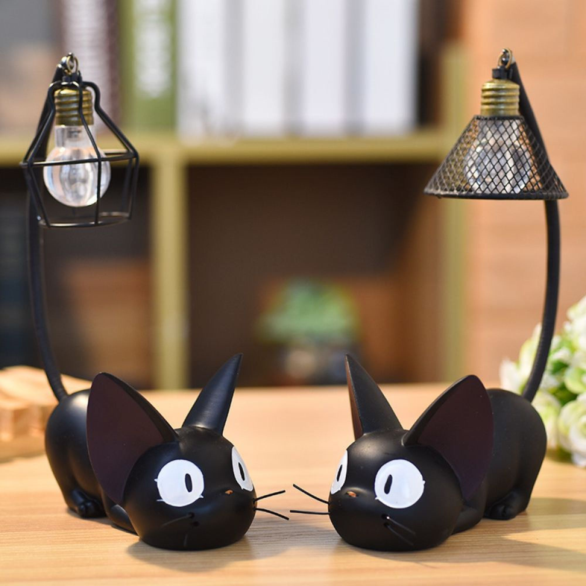 Zwei schwarze Katzenfiguren face einander, mit Lampen an ihren gebogenen Schwänzen auf einer Holzoberfläche.