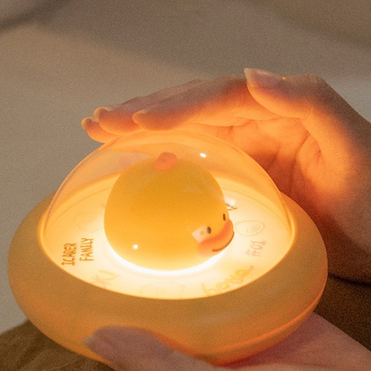 Eine Hand berührt sanft ein gelbes, UFO-förmiges Nachtlicht mit einer süßen Ente.