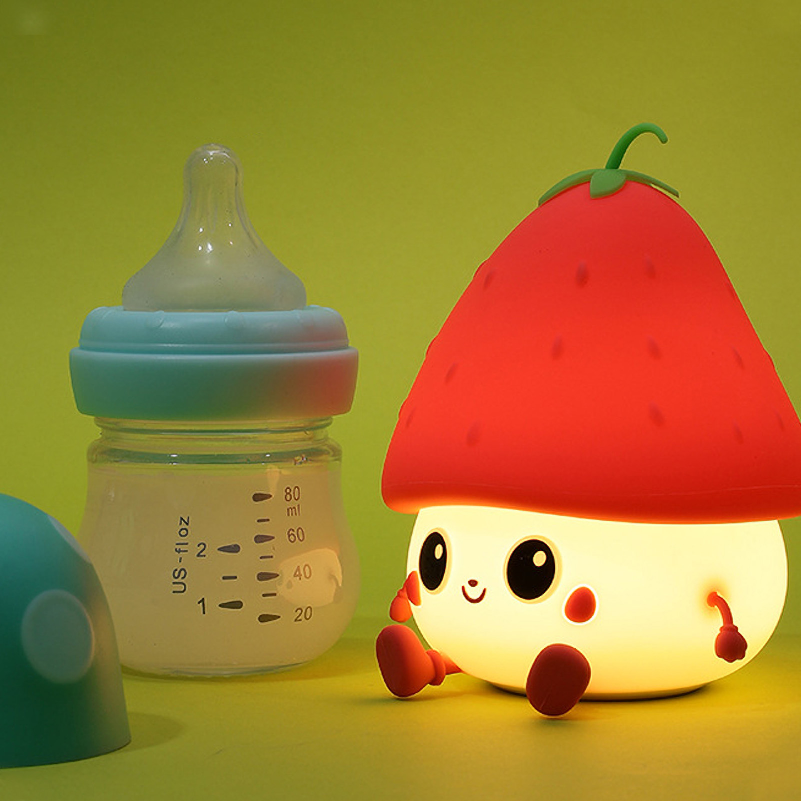 Eine Babyflasche neben einer leuchtenden, süßen erdbeerförmigen Lampe vor grünem Hintergrund.
