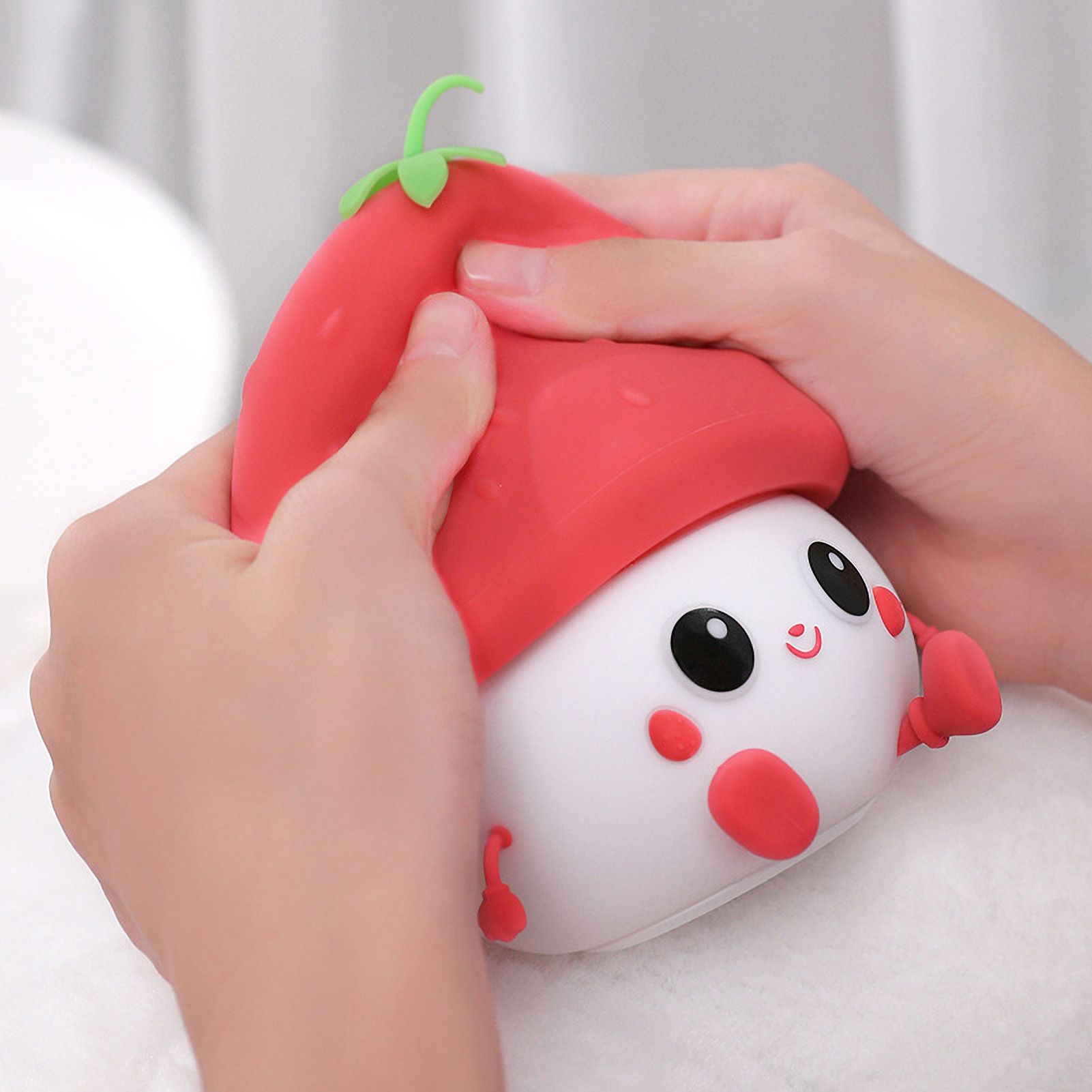 Hände drücken einen roten, erdbeerförmigen Silikon-Anti-Stressball mit niedlichem Gesicht.
