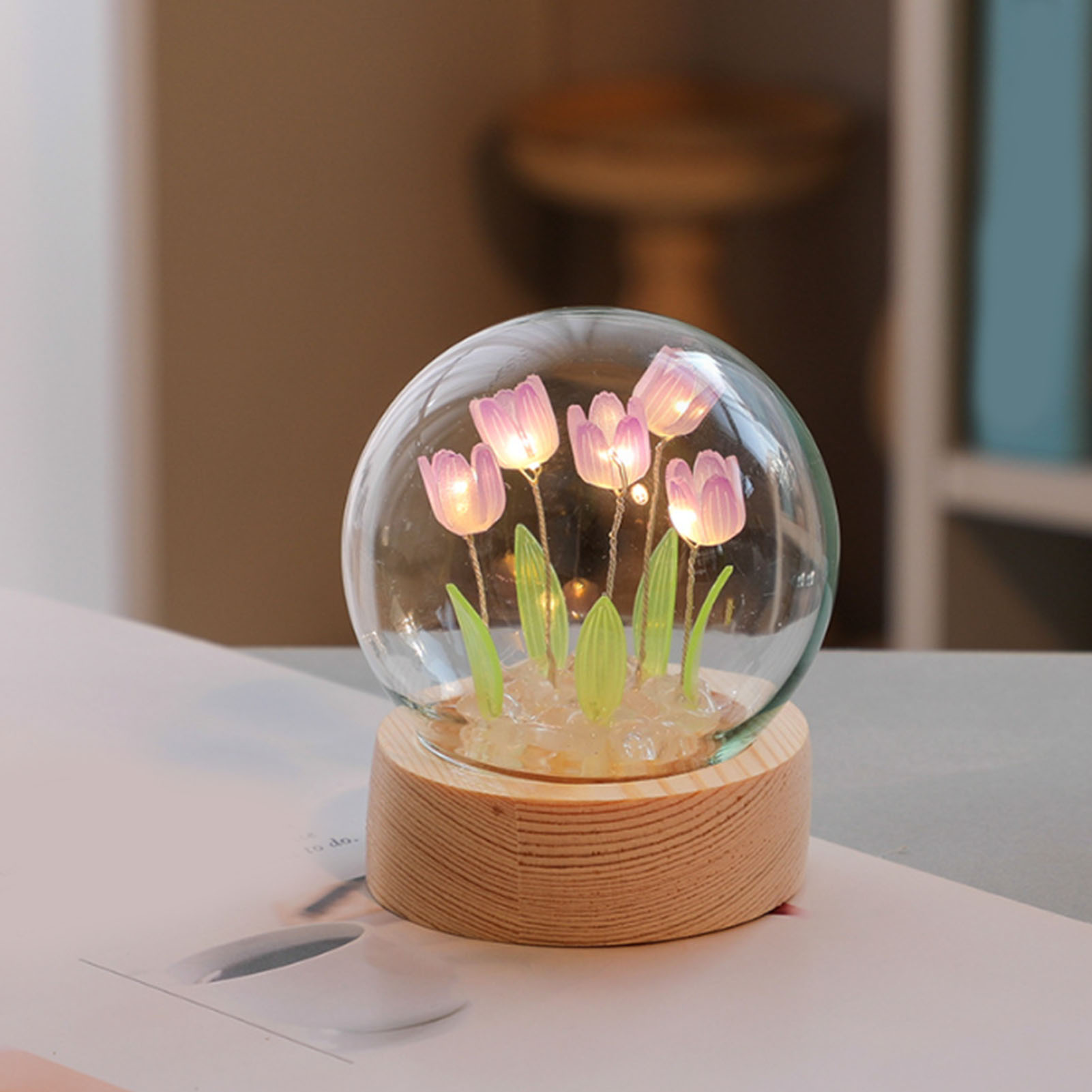 Eine Glaskugel mit beleuchteten Tulpen auf einem Holzsockel auf einem Tisch.