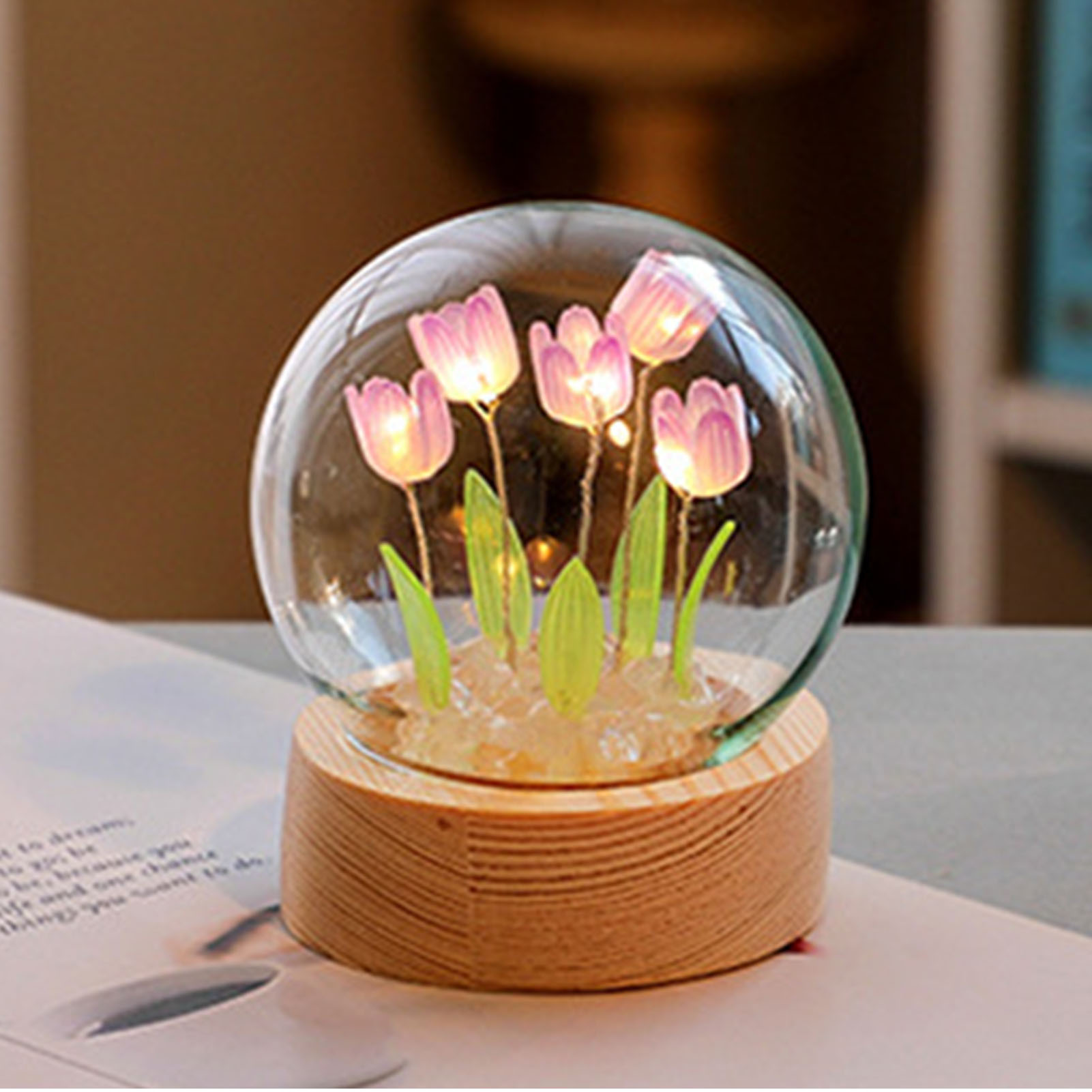 Eine kleine Glaskugel auf einem Holzsockel enthält leuchtende rosafarbene Tulpen und grüne Blätter.