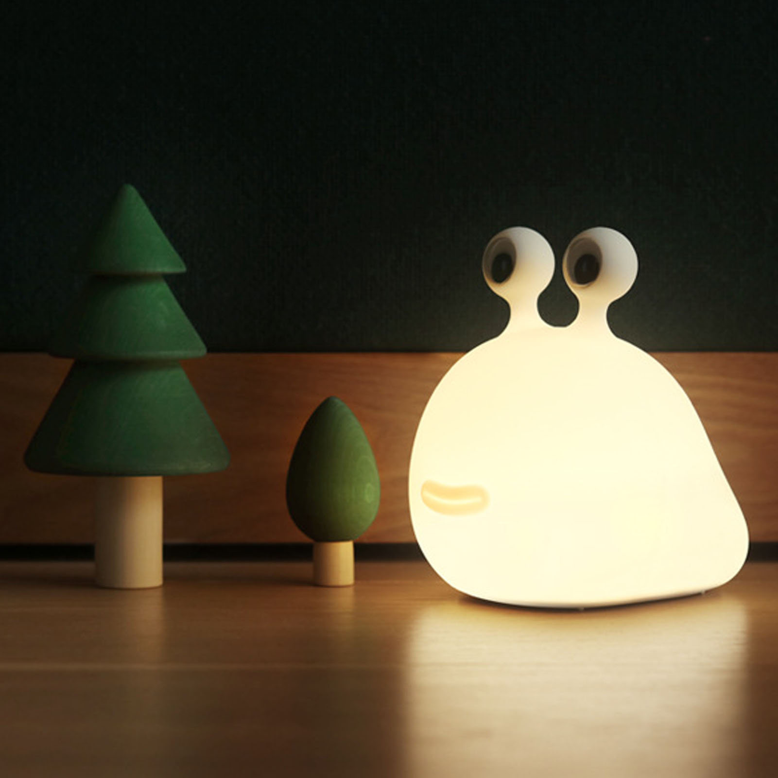 Eine leuchtende Schneckenlampe steht neben zwei kleinen Holzbäumen auf einer Holzoberfläche.