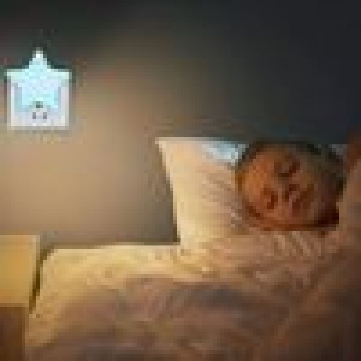 Ein Kind schläft im Bett unter einer Decke, während ein leuchtendes Stern-Nachtlicht an der Wand steckt.