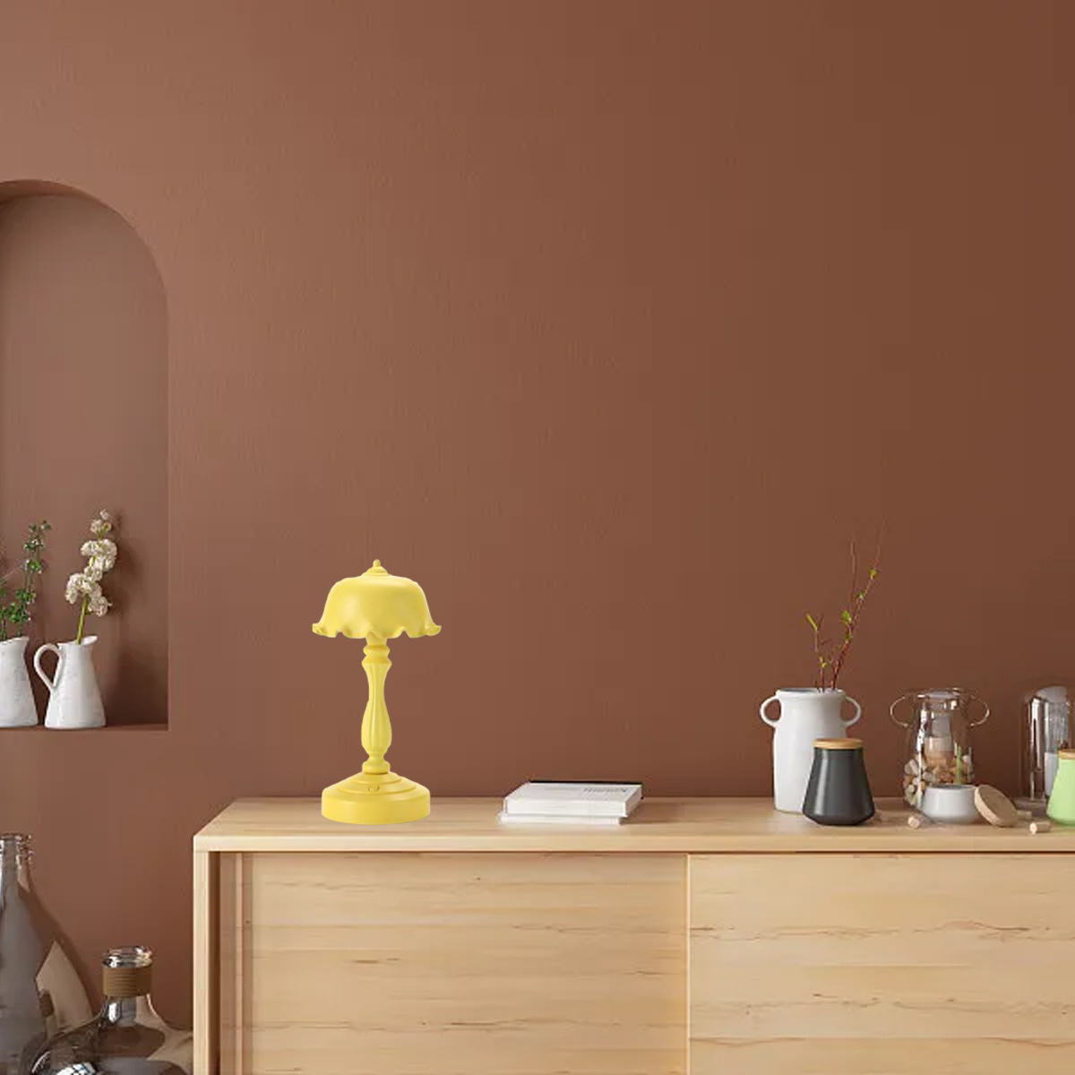 Eine gelbe Lampe, Bücher und Vasen stehen auf einem hellen Holzsitzmöbel vor einer braunen Wand.