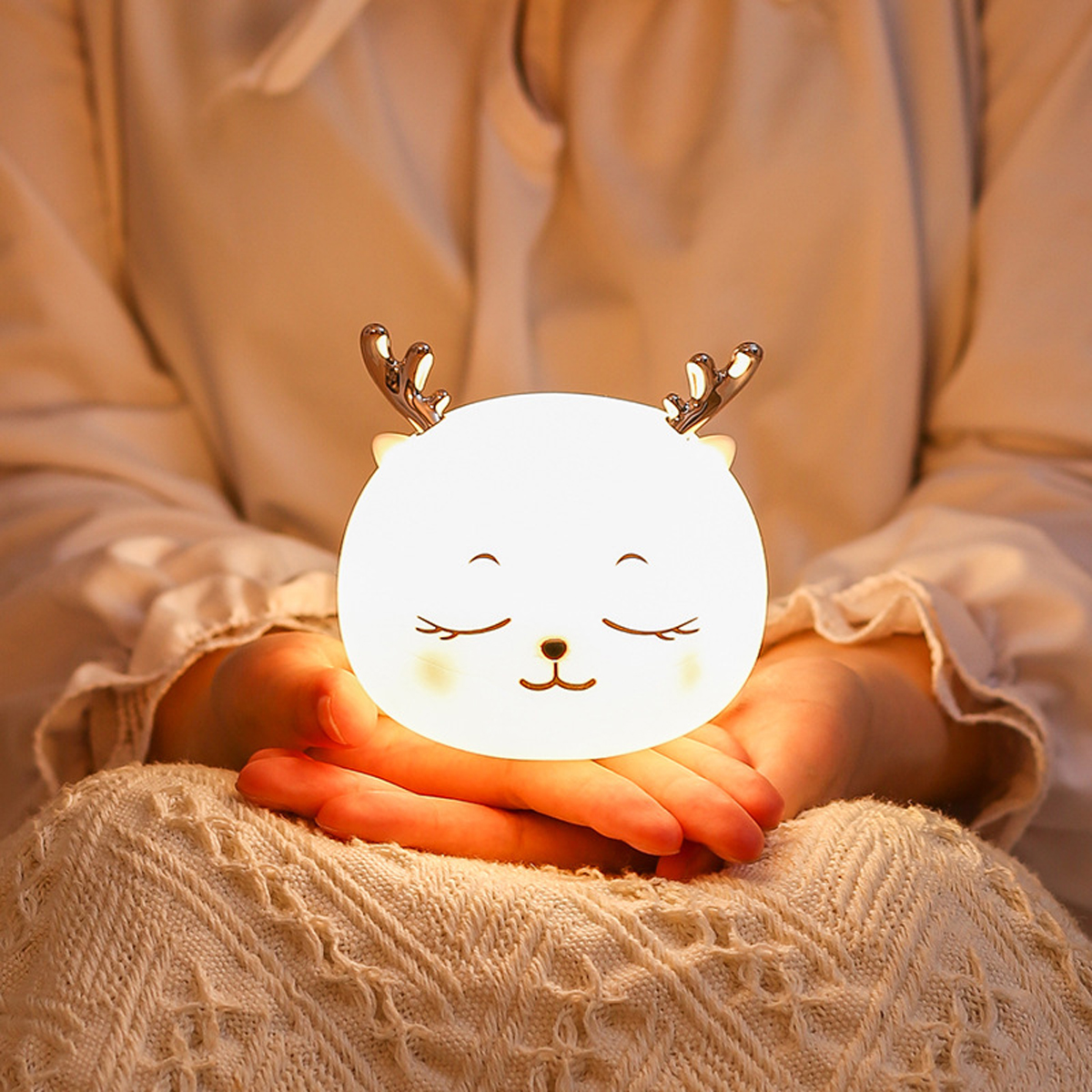 Person hält eine kleine, leuchtende Reh-Nachtlampe mit schlafendem Gesicht.