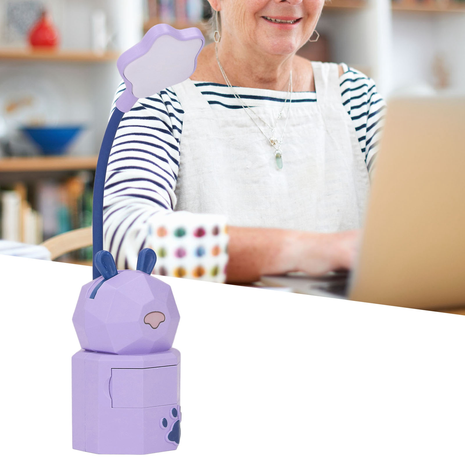 Eine lila Hasen-Schreibtischlampe steht auf einem Tisch, während eine ältere Frau am Laptop arbeitet.