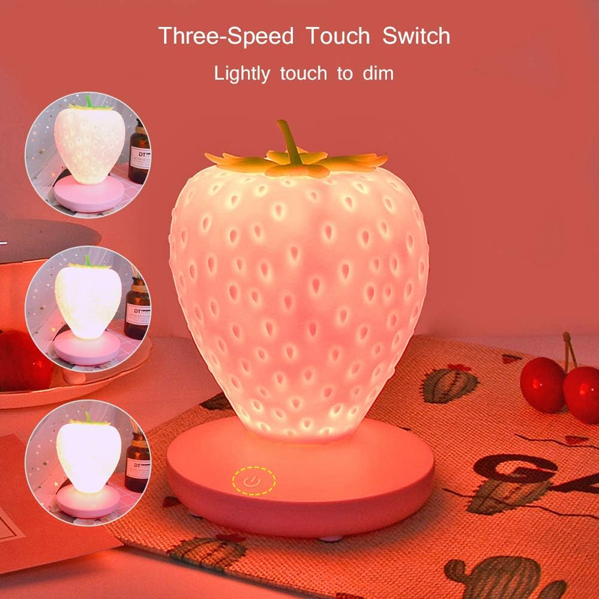 Eine rosa erdbeerförmige Nachttischlampe auf einem Tisch mit zwei roten Kirschen.