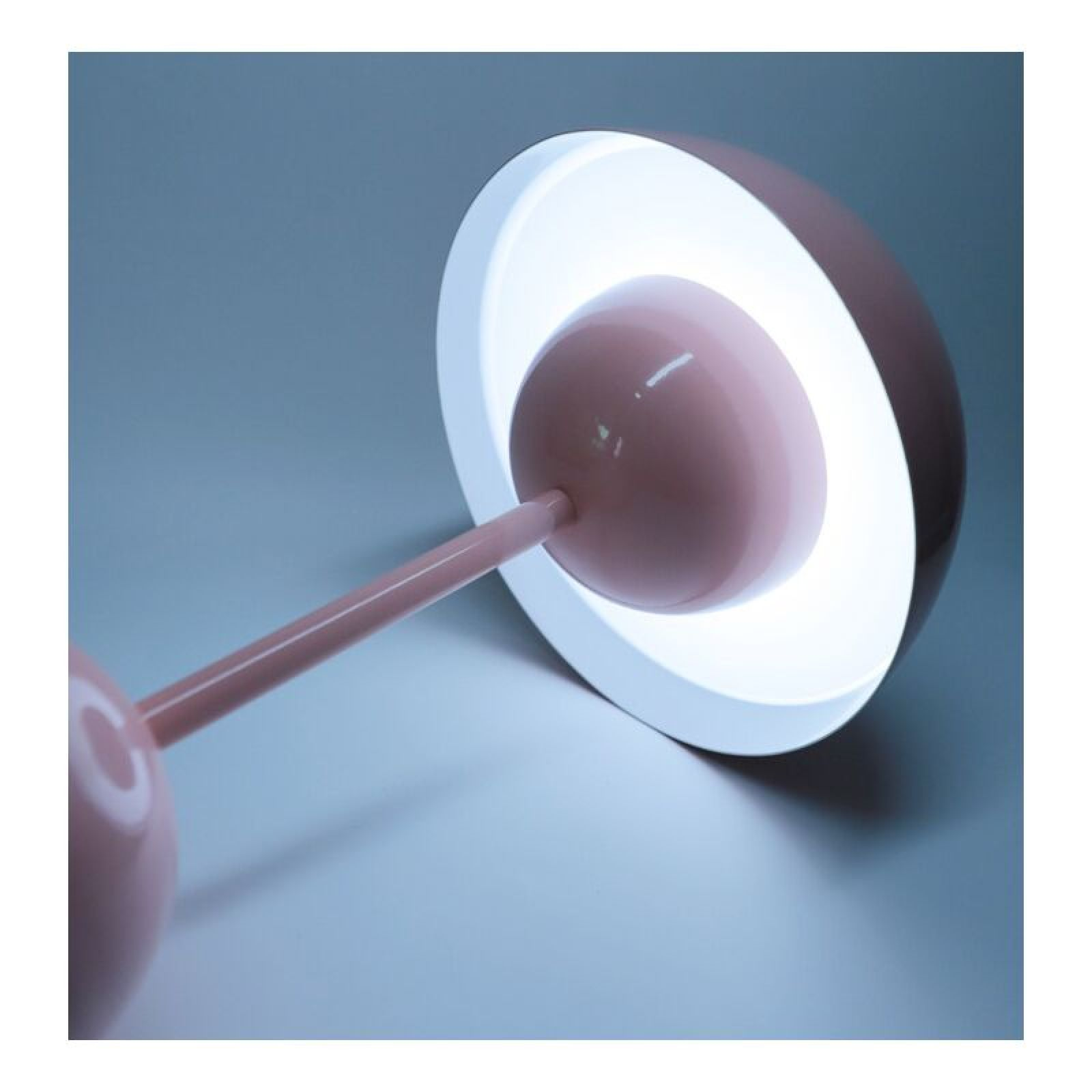 Eine moderne rosa-weiße Schreibtischlampe leuchtet hell vor dunklem Hintergrund.