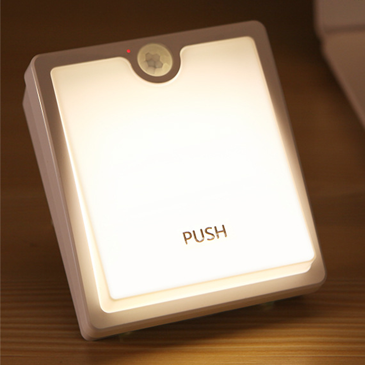 Eine quadratische, weiße LED-Wandleuchte mit der Aufschrift PUSH und einem oberen Sensor auf einer Holzoberfläche.