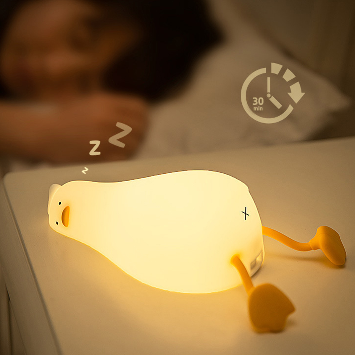 Eine glühende Enten-Nachtlampe liegt auf einem Nachttisch, während eine Person im Hintergrund schläft.