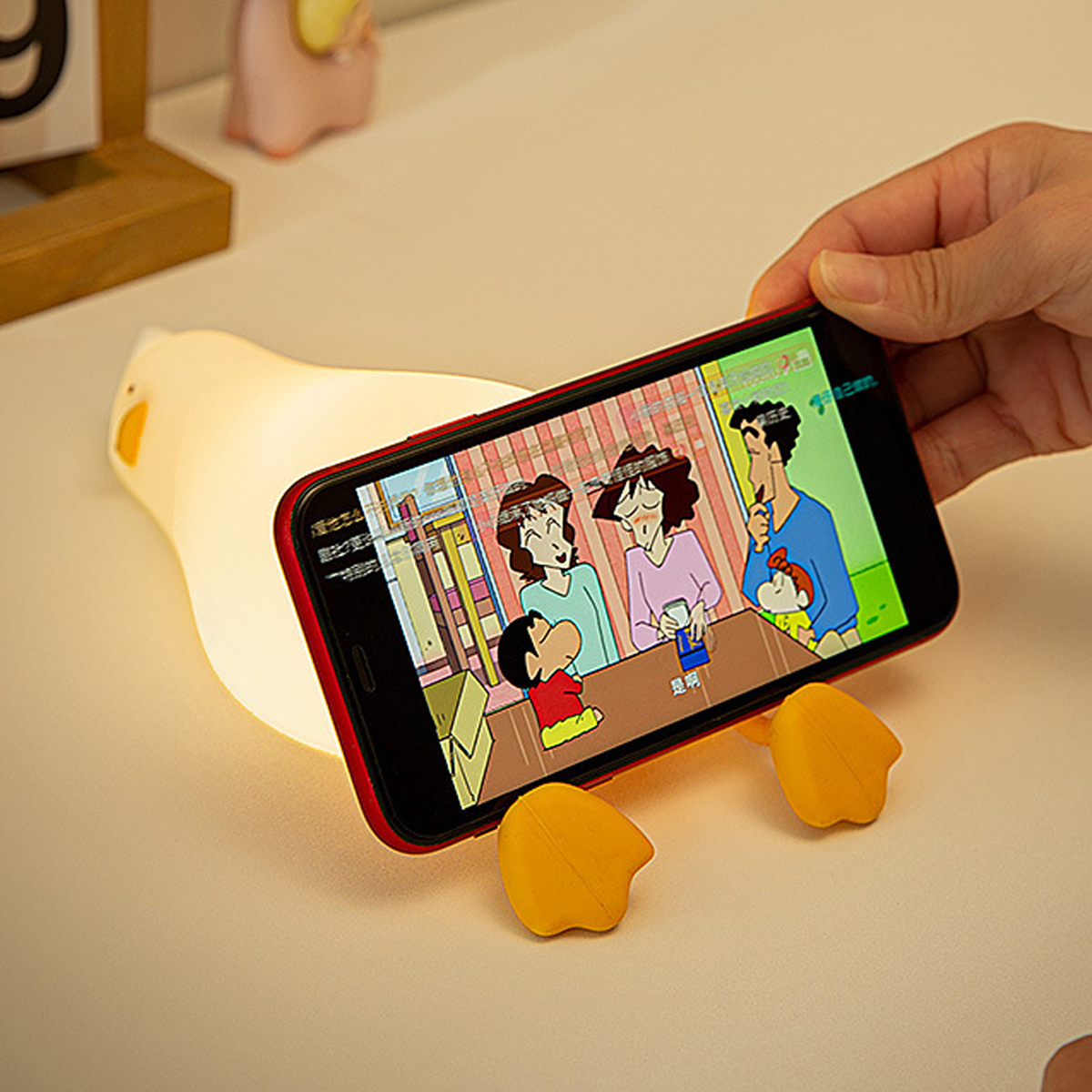 Eine Hand hält ein Smartphone mit einem Cartoon auf einer entenförmigen Nachtlampe und Handyhalterung.