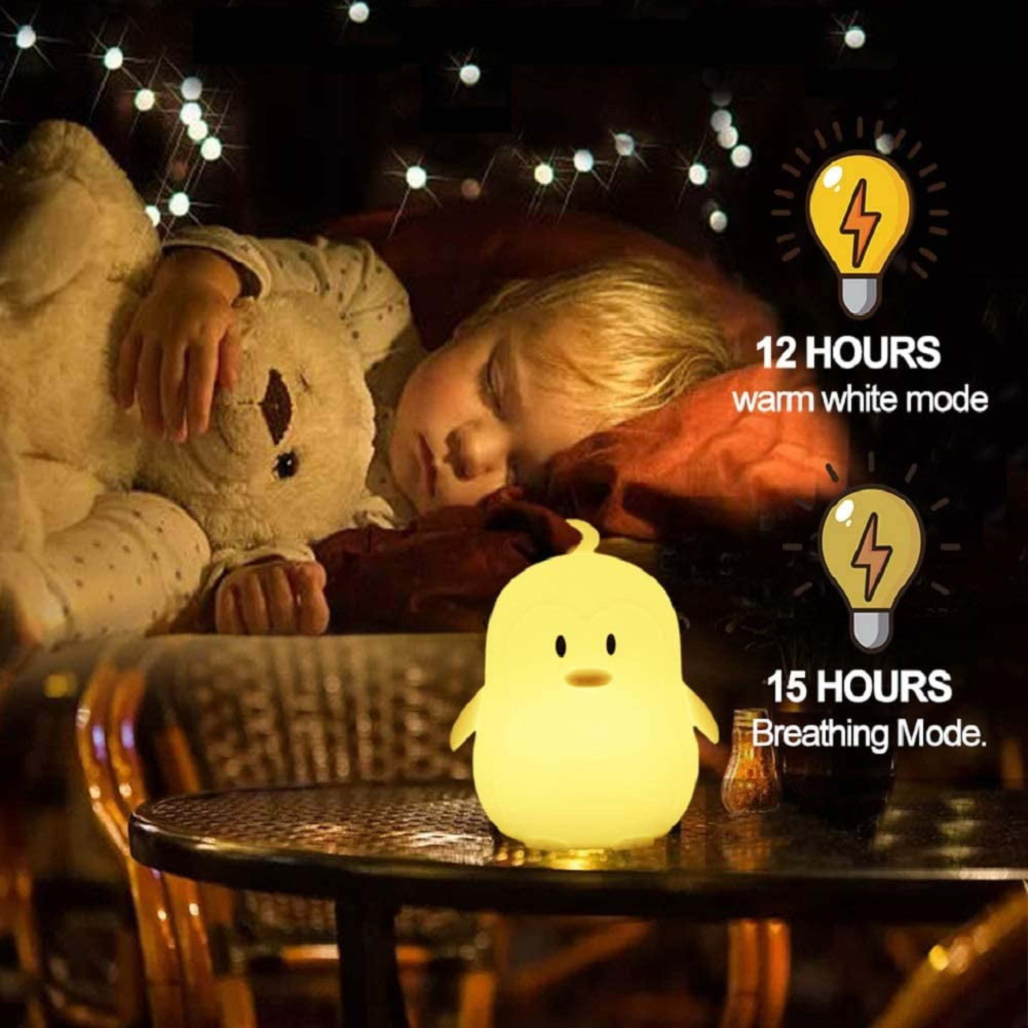 Ein gelbes Küken-Nachtlicht steht auf einem Tisch, während ein Kind mit Teddybär schläft.