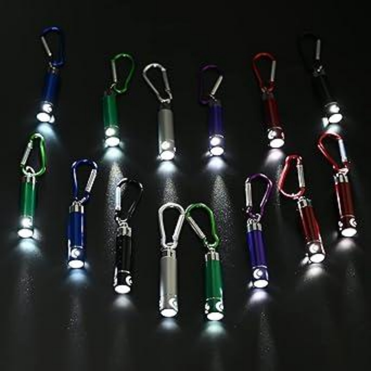 Bunte Minitaschenlampen mit Karabinerhaken sind auf einer dunklen Oberfläche angeordnet und leuchten.