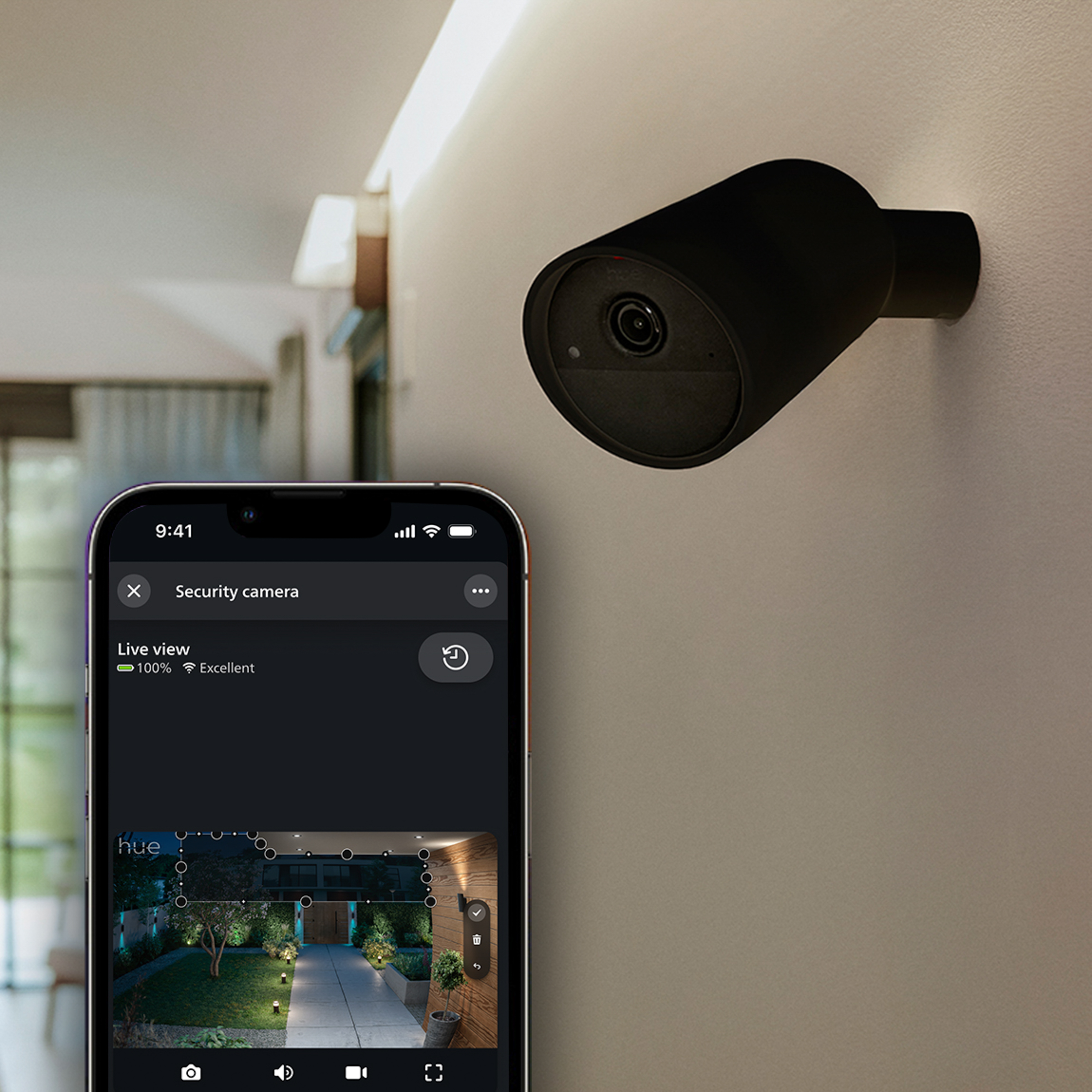 Telecamera di sicurezza nera su parete chiara e smartphone con vista dal vivo.