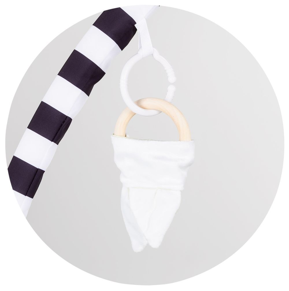 Ein Babyspielzeug hängt an einem schwarz-weiß gestreiften Bogen mit Holzring und weißem Tuch.