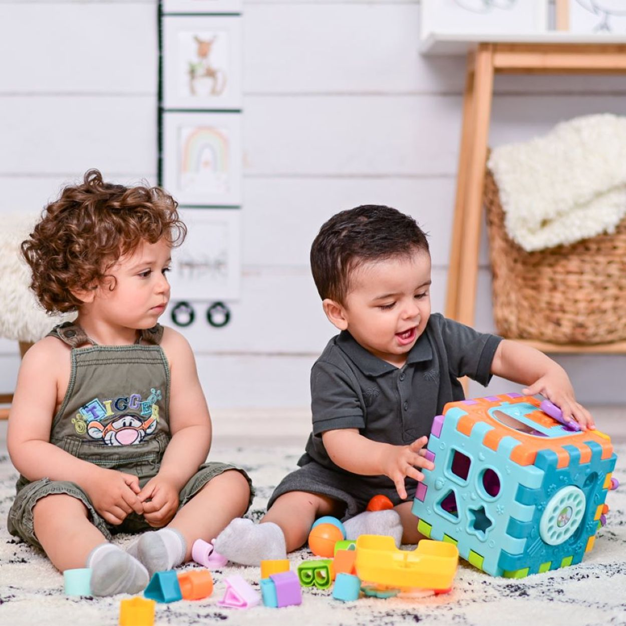 Zwei kleine Jungen spielen auf einem Teppich mit einem bunten Sortierwürfel und Spielzeug.
