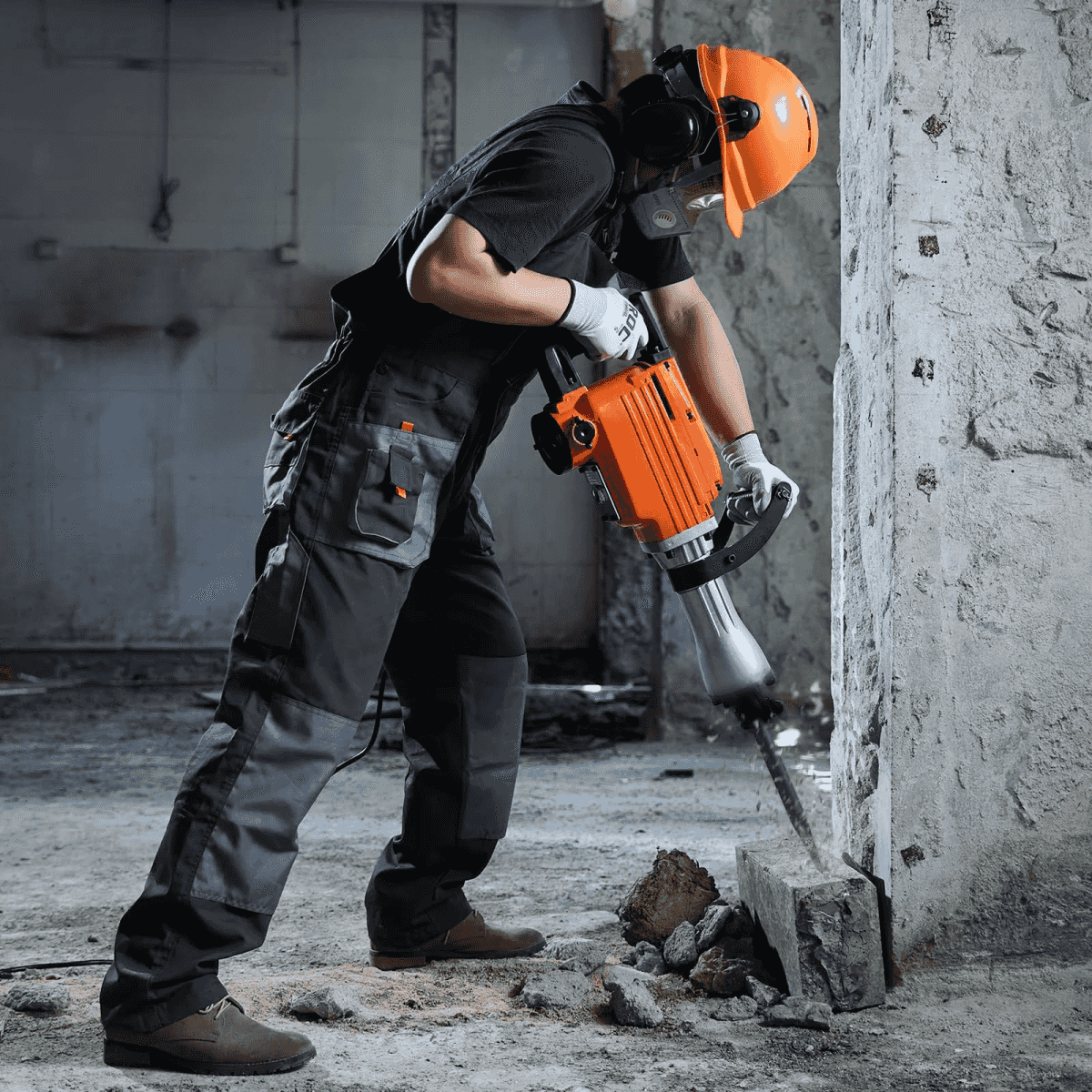 Un trabajador con equipo de protección usa un martillo neumático naranja para romper un muro de hormigón.