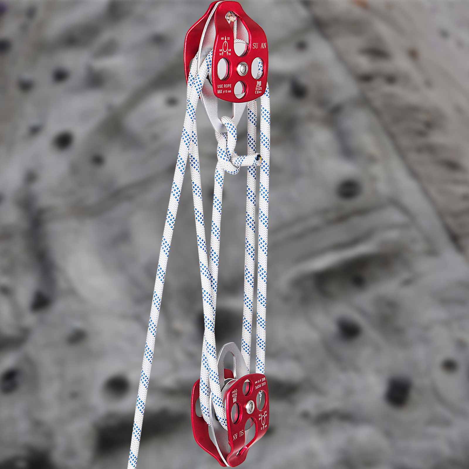 Poleas de escalada rojas y plateadas con cuerdas blancas y azules contra un muro difuminado.
