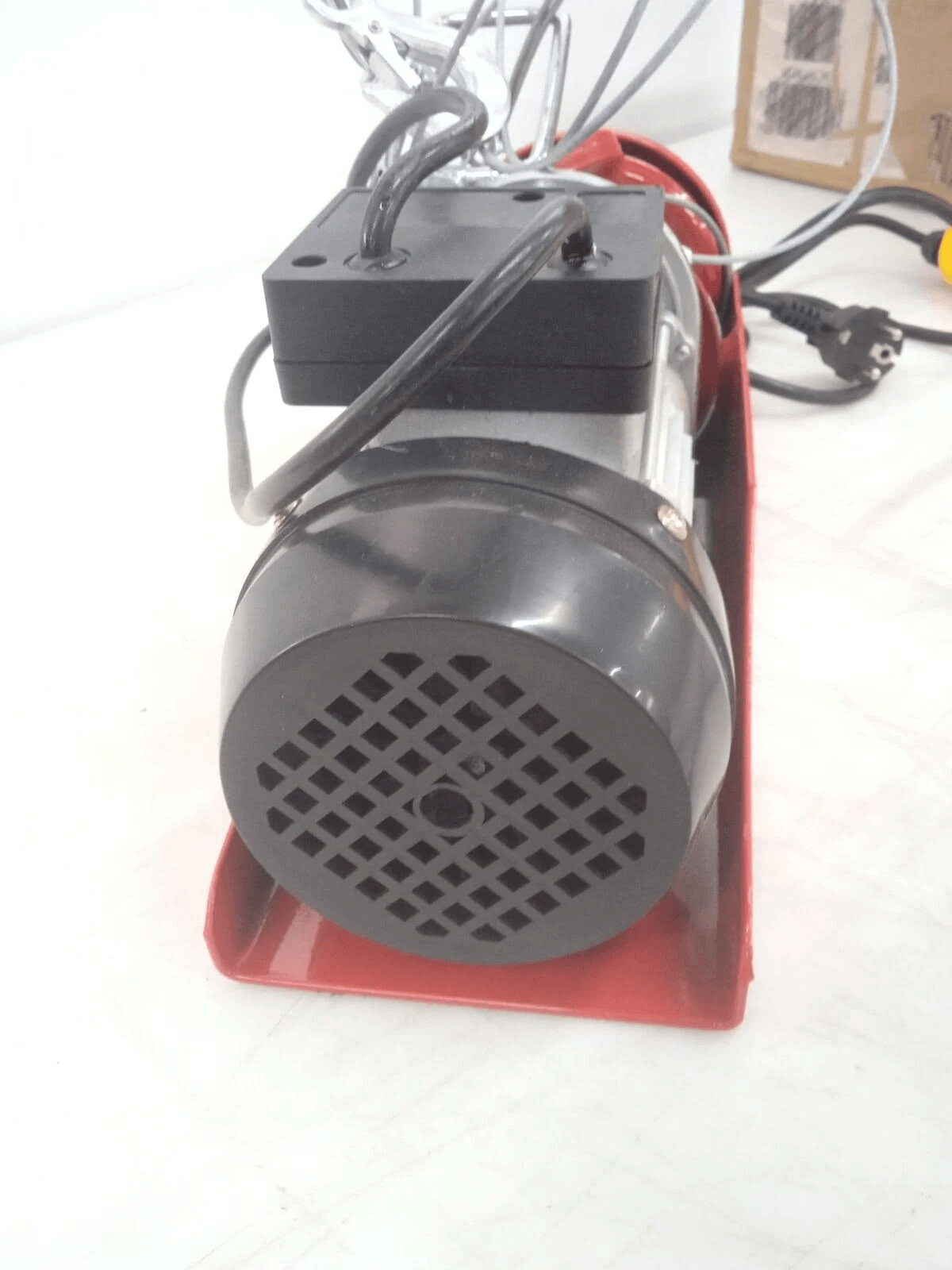 Un motor eléctrico rojo y negro con cables se encuentra sobre una superficie blanca.