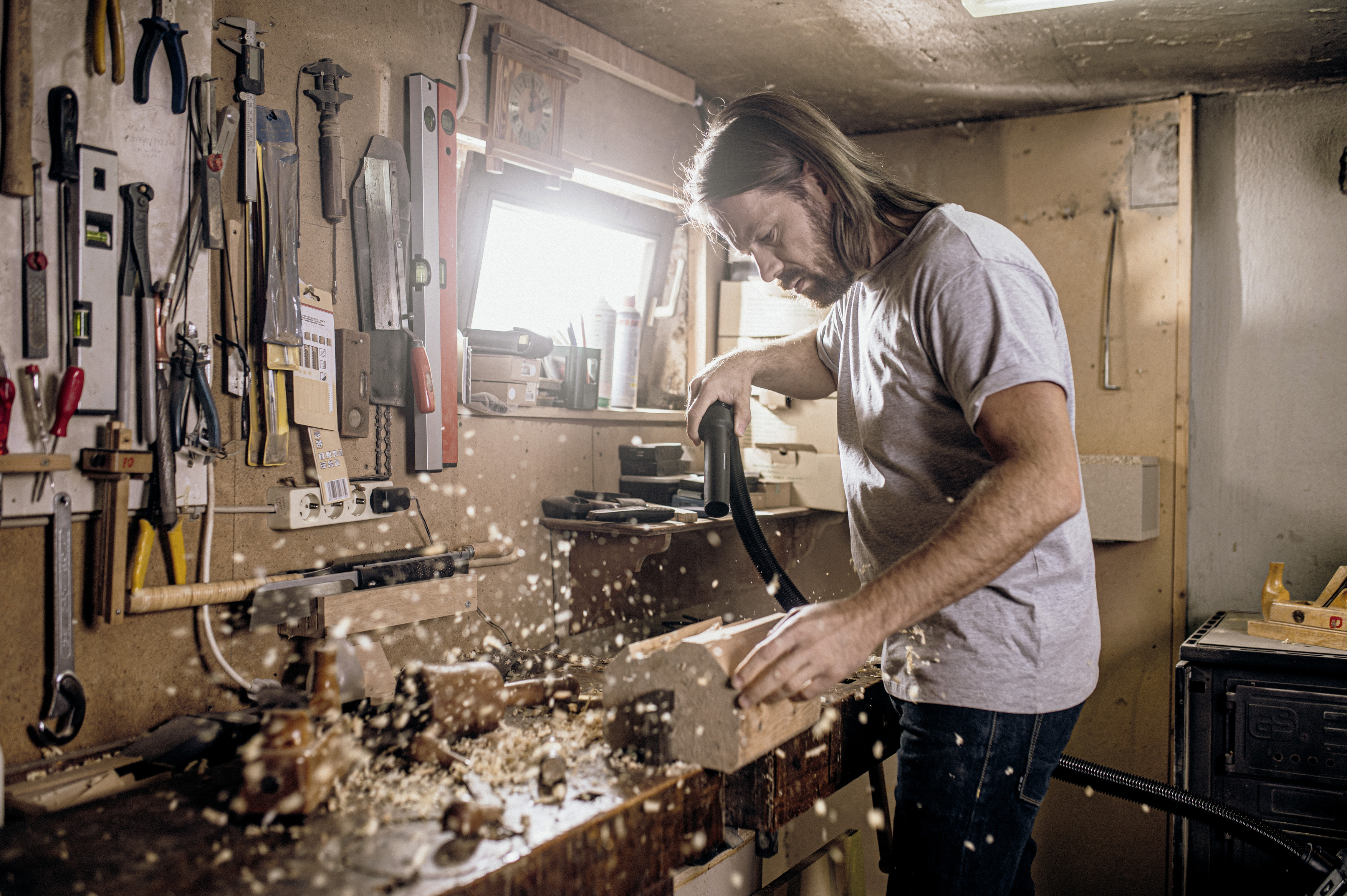 Un artesano de pelo largo aspira virutas de madera en un taller bien equipado.