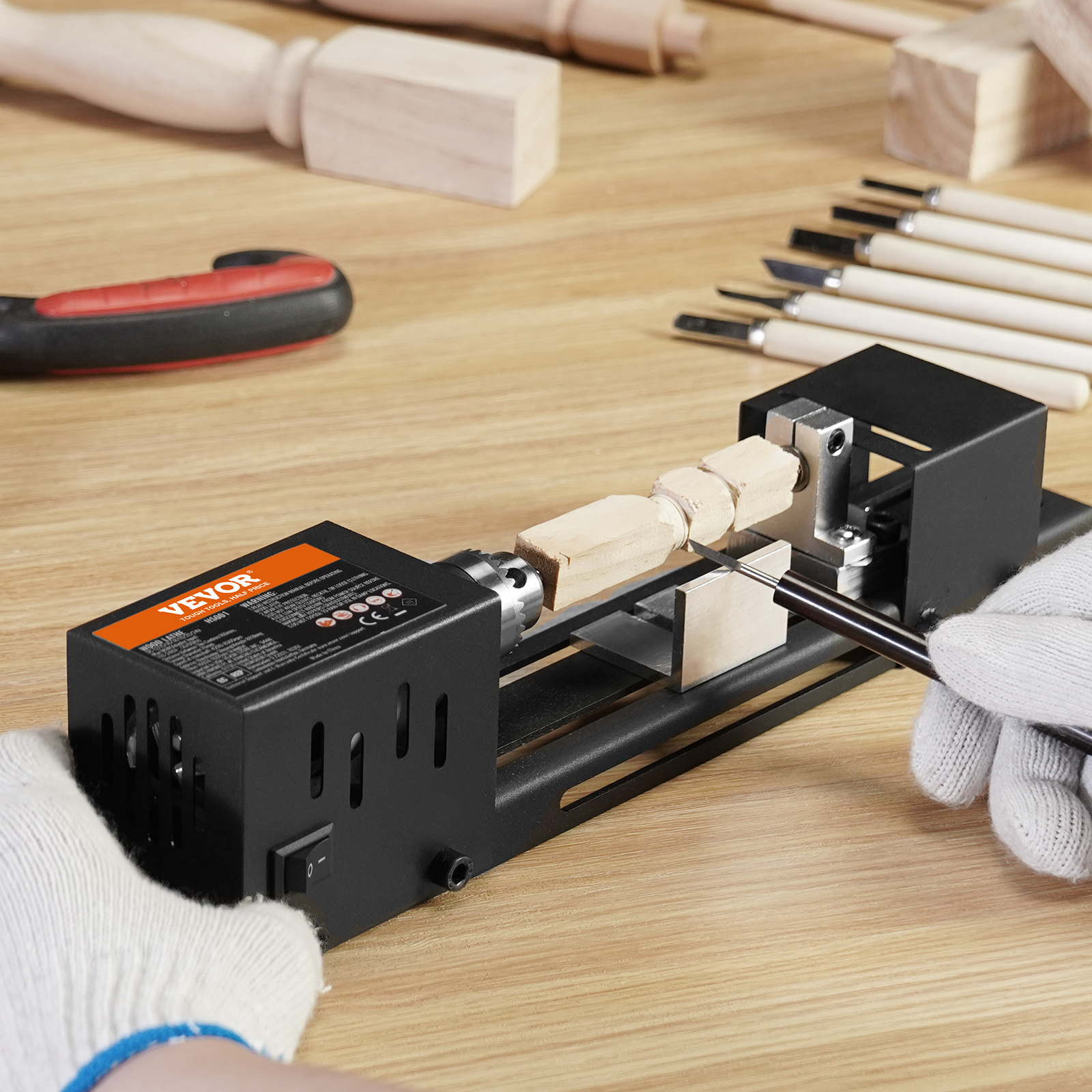Una persona con guantes usa un mini torno para dar forma a madera en un banco de trabajo.