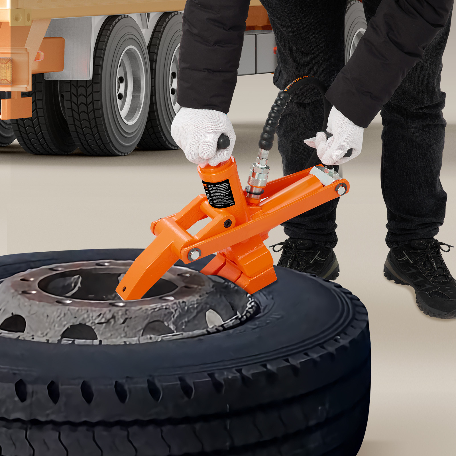 Una persona con guantes blancos usa una herramienta hidráulica naranja para desmontar un neumático de camión.