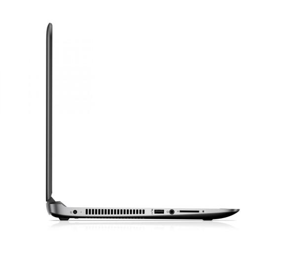 Seitenansicht eines geschlossenen grauen Laptops mit sichtbaren Anschlüssen und Lüftungsschlitzen auf einer weißen Fläche.