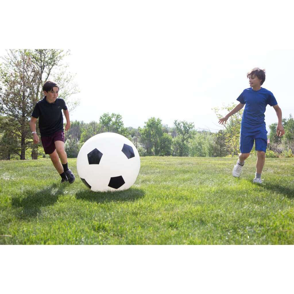 Zwei Jungen spielen auf einer grünen Wiese draußen Fußball mit einem riesigen Ball.