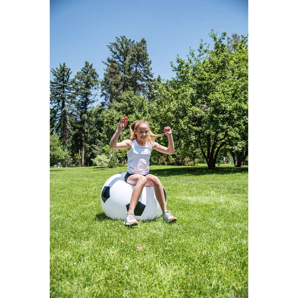 Ein junges Mädchen sitzt auf einem großen Fußball in einem sonnigen Park.