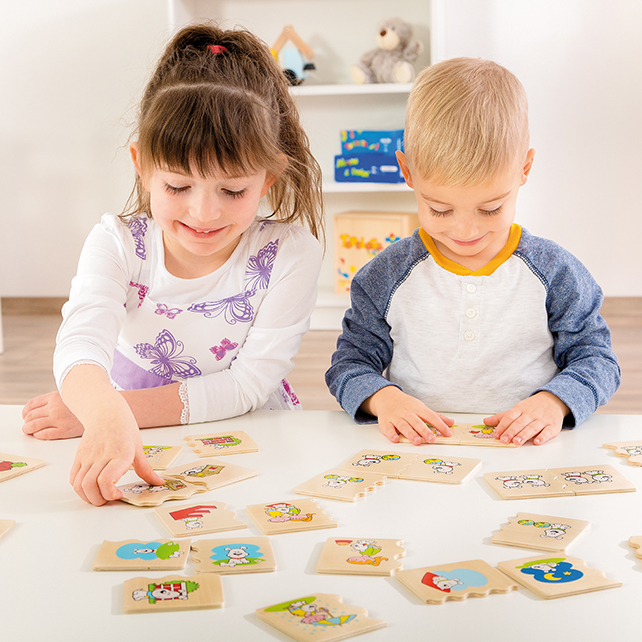 Una niña y un niño se sientan a una mesa blanca, sonriendo mientras juegan con piezas de rompecabezas.