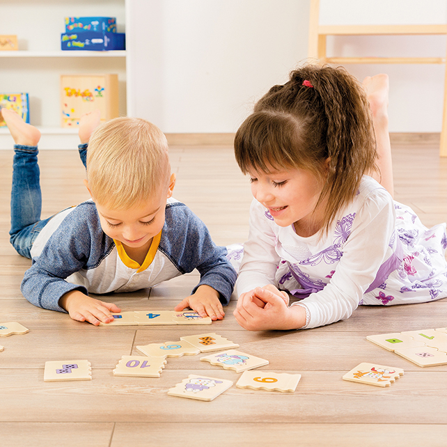 Dos niños yacen en un suelo de madera, jugando con tarjetas didácticas y rompecabezas de números.