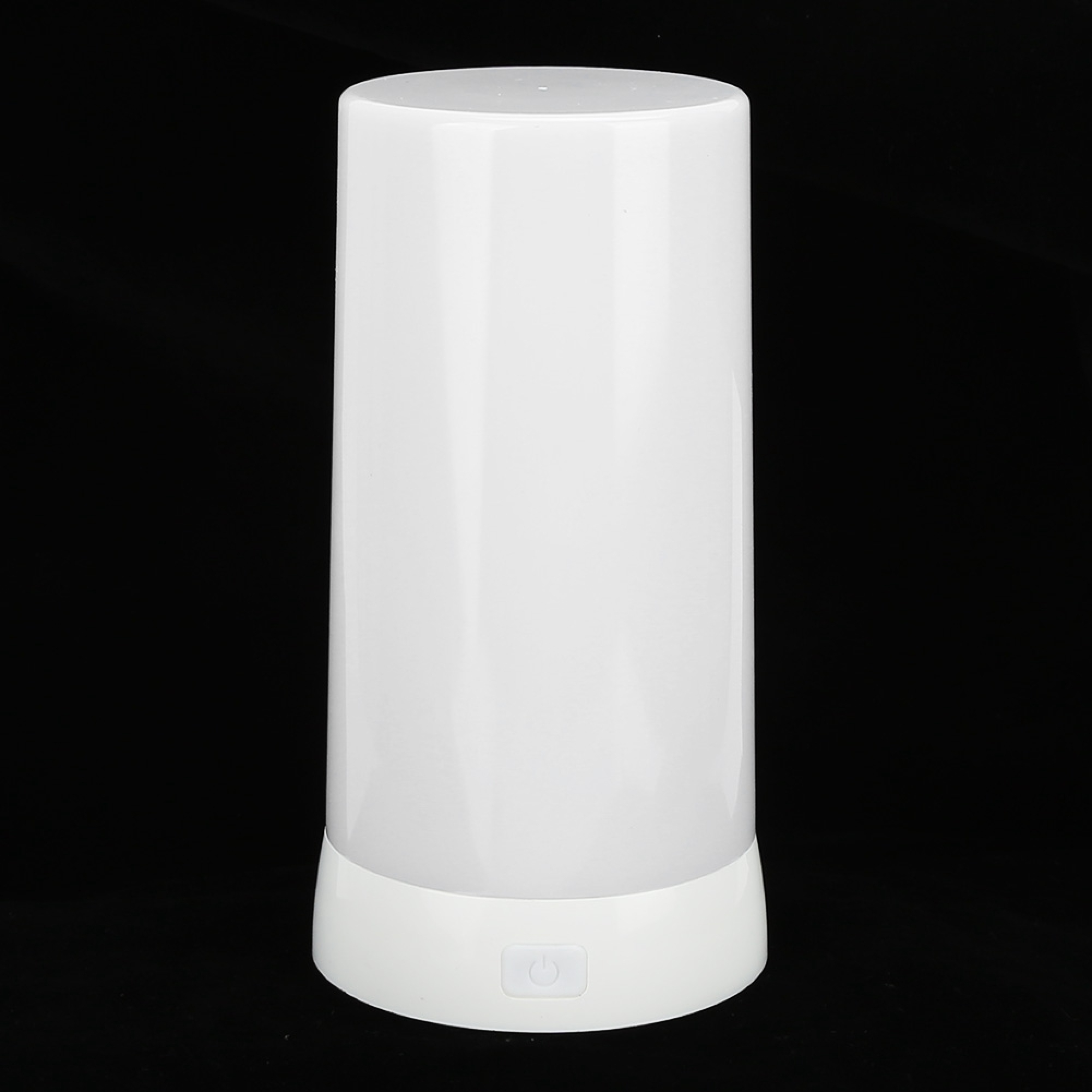 Eine zylindrische weiße Lampe mit einem flachen Boden und einem Netzschalter vorne steht auf schwarzem Hintergrund.