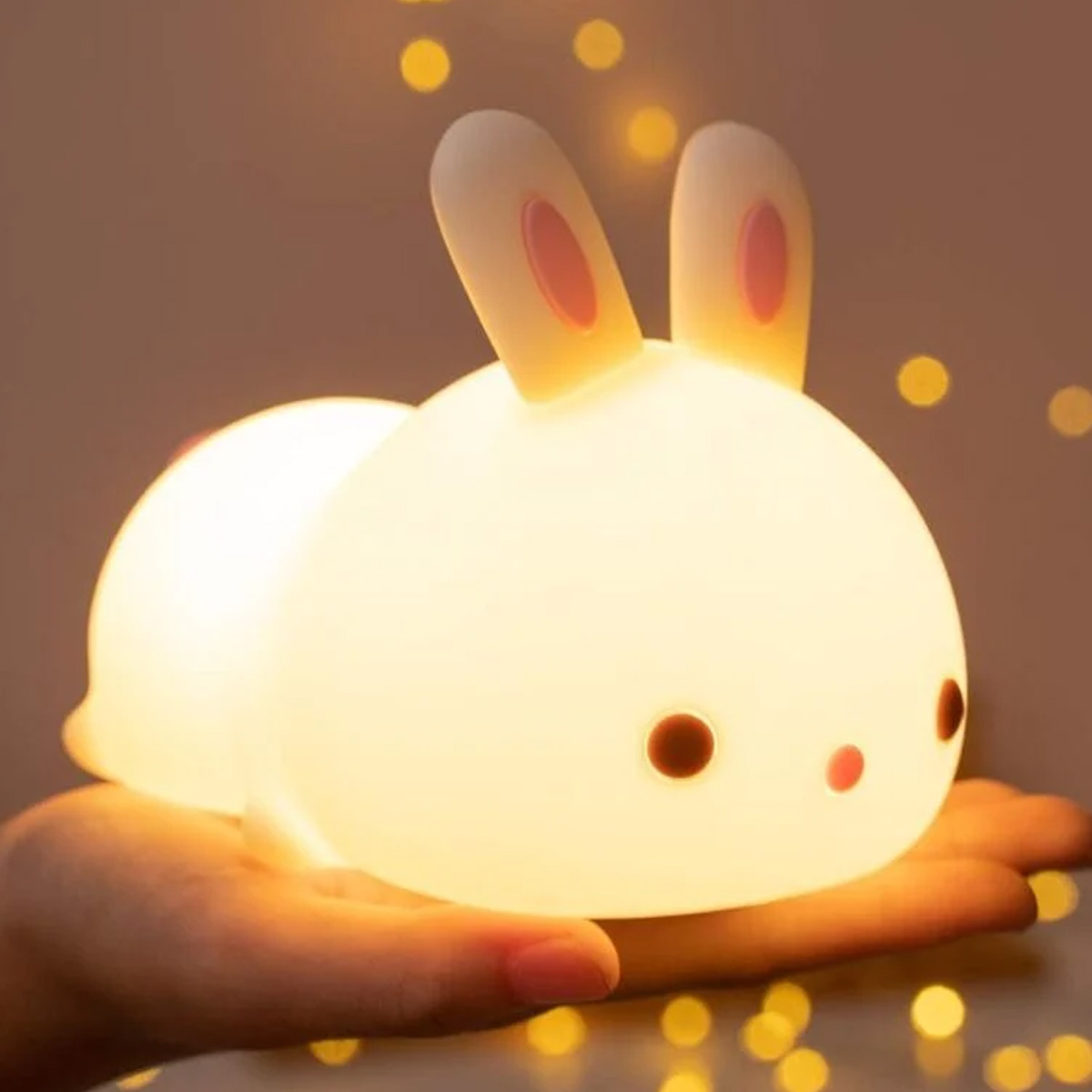 Eine Hand hält eine kleine, leuchtend weiße Hasenlampe mit rosa Ohren.