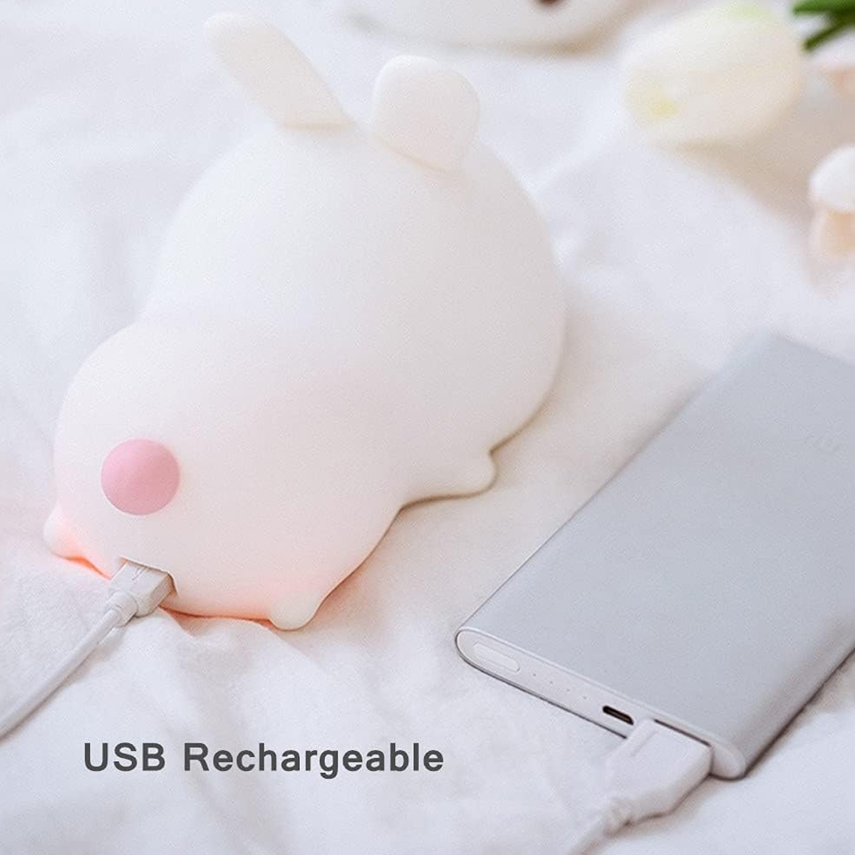 Ein süßes weißes Kaninchen-Nachtlicht ist per USB-Kabel an eine Powerbank auf weißer Oberfläche angeschlossen.