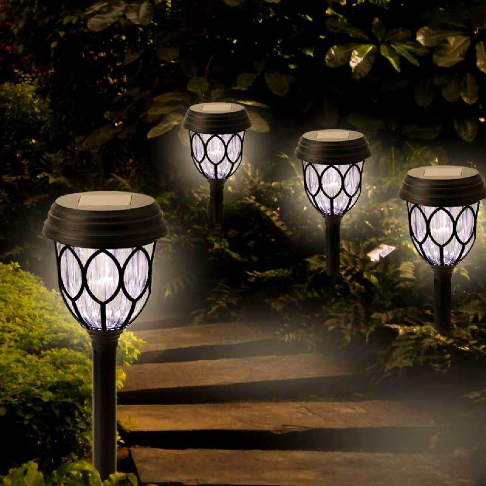 Vier solarbetriebene Gartenlampen beleuchten abends einen dunklen Gartenweg.