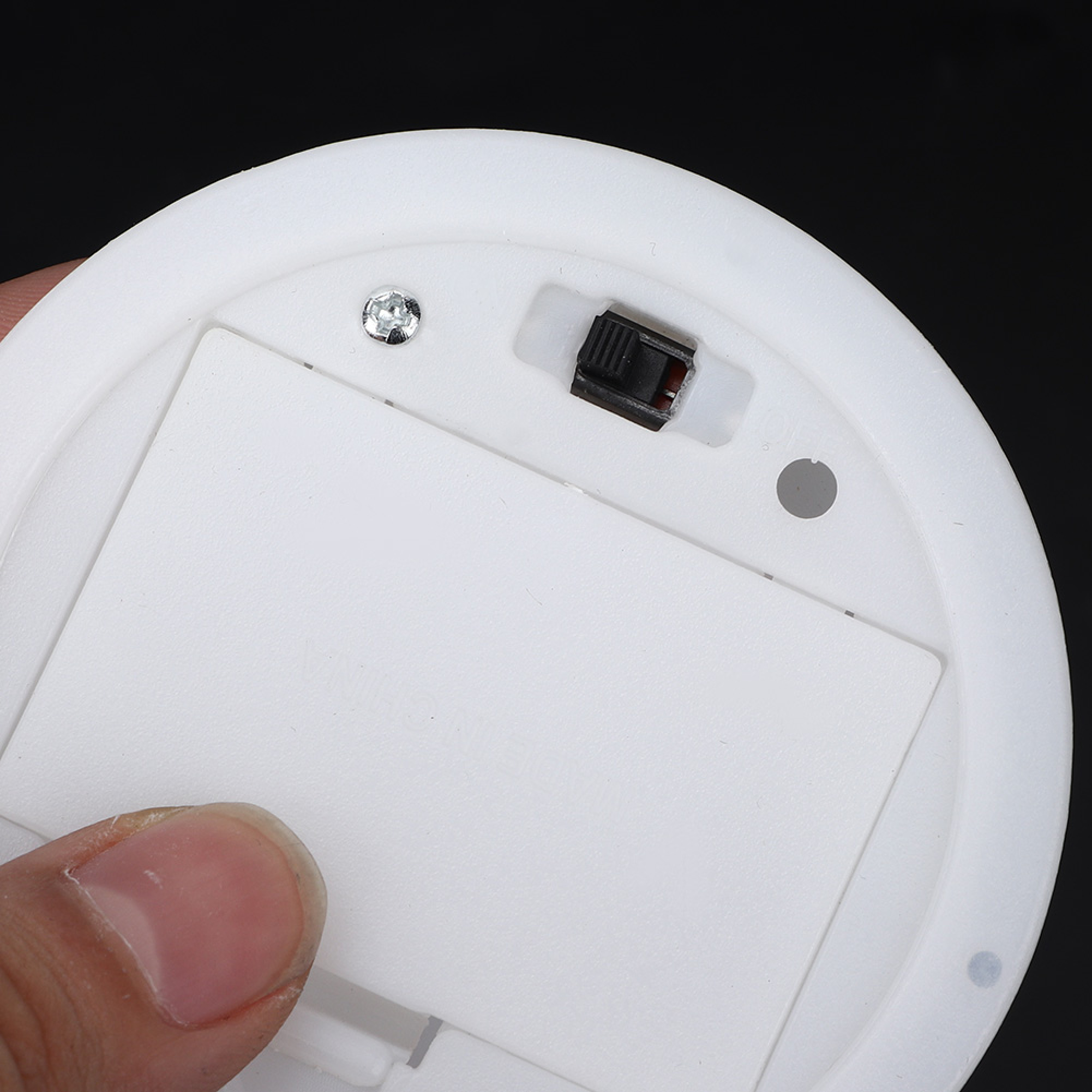 Unterseite eines runden weißen Geräts mit Batteriefach, Schalter und Schraube.
