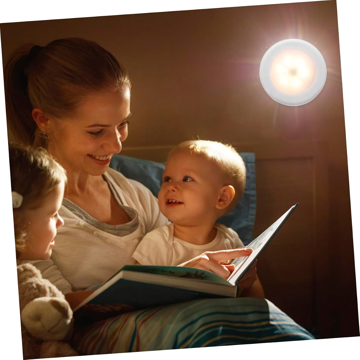 Mutter liest ihren zwei Kindern im Bett ein Buch, beleuchtet von einer Wandlampe.